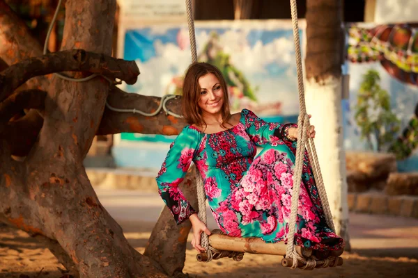 Chica delgada en largos columpios con los ojos cerrados contra la planta tropical —  Fotos de Stock