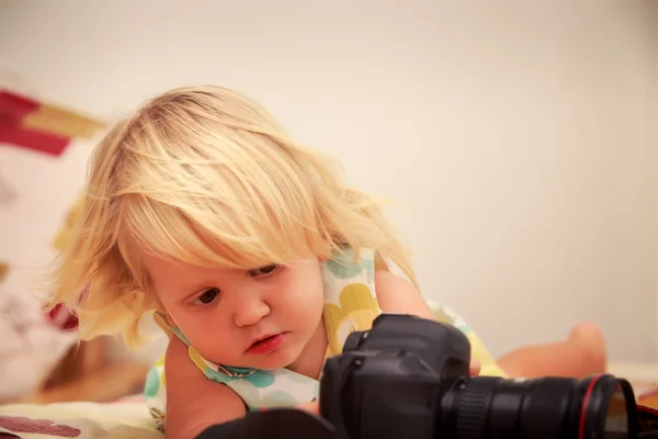 Little blonde girl looks into camera on sofa against white wall — Stock Photo, Image