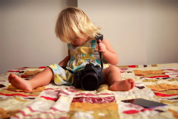 Little blonde girl tries to put on camera against white wall — Stock Photo, Image
