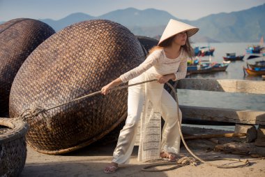 blonde girl in Vietnamese dress pulls rope on embankment