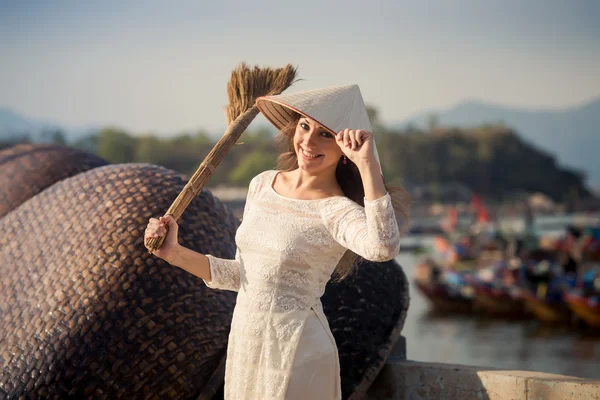 Chica rubia en vestido vietnamita sostiene besom en terraplén —  Fotos de Stock