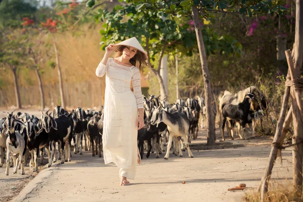 Blonde girl in Vietnamese dress stands against flock — Stock fotografie