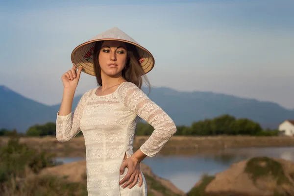 Блондинка во вьетнамском платье улыбается сельским озерам — стоковое фото