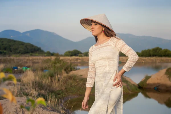 Blonde girl in Vietnamese dress smiles against country lakes — Stock Photo, Image