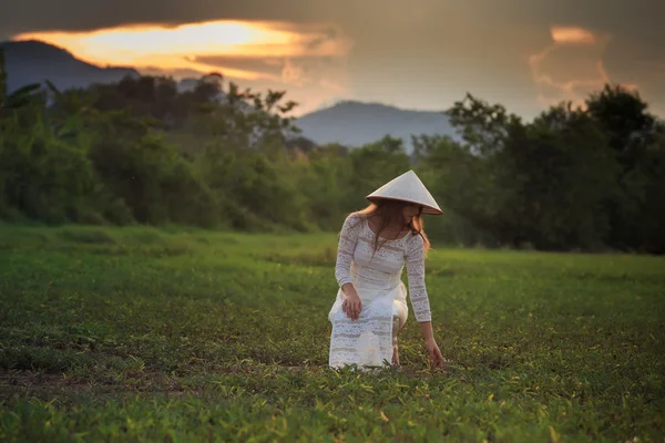 Blonde girl in Vietnamese dress squats on grass field — Stock fotografie