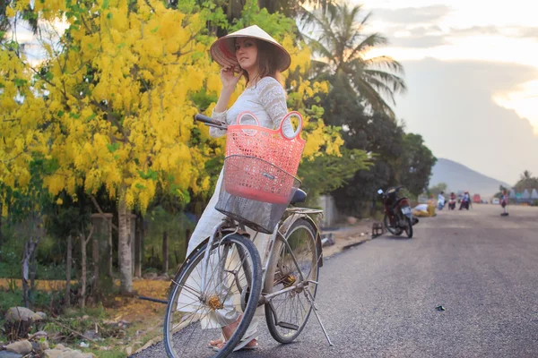 Menina loira em vestido vietnamita e chapéu perto de bicicleta na rua — Fotografia de Stock