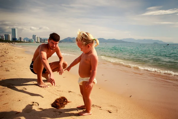 Father shows seaweed to little daughter on sand beach — Stock Photo, Image