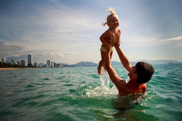 Father tosses up laughing little daughter above sea water — Stock Photo, Image