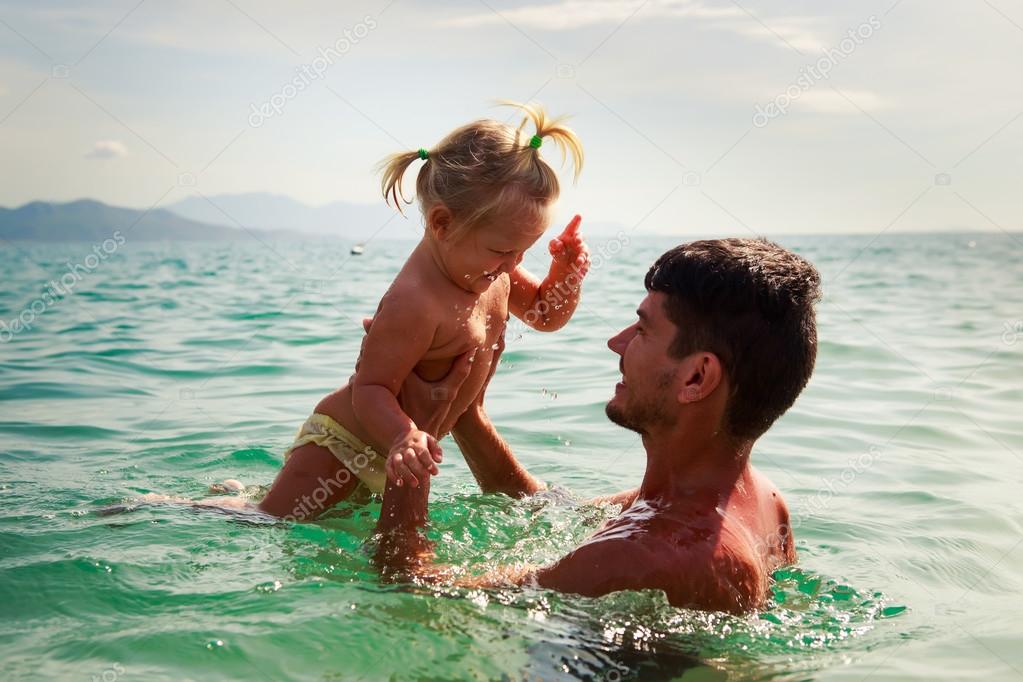 Pai joga-se sorrindo pequena filha acima da agua do mar fotos, 