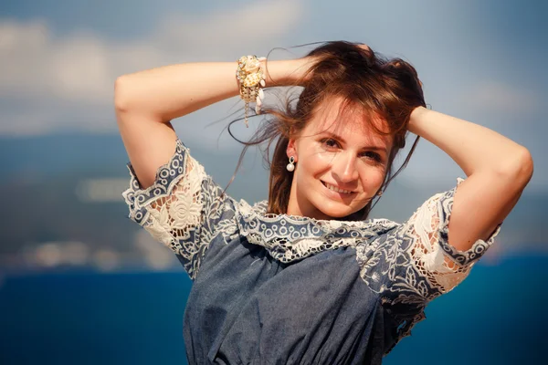 Brunette girl in grey frock smiles against defocused sea — Stock fotografie