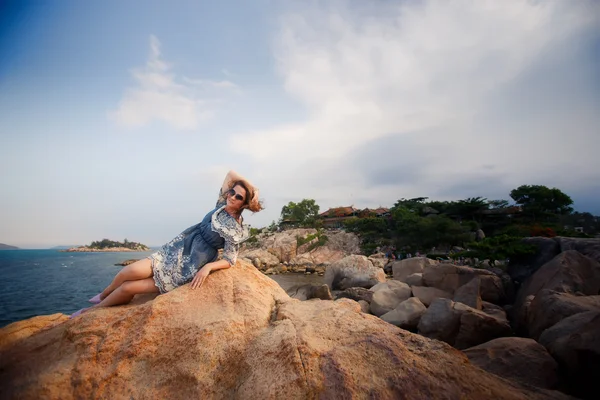 Девушка в коротком сером платье лежит на скале против камней растений — стоковое фото