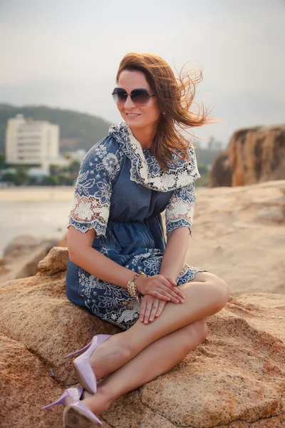 Girl in short grey frock sits on rock shows legs against city — Stock fotografie