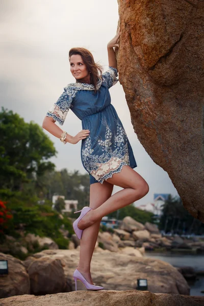 Brunette girl in short frock high-heel shoes stands under rock — Stockfoto