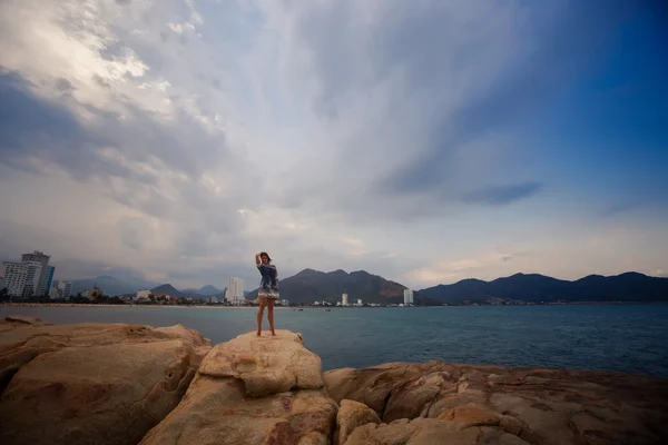 Vista de chica en vestido corto sobre rocas a distancia contra el mar —  Fotos de Stock