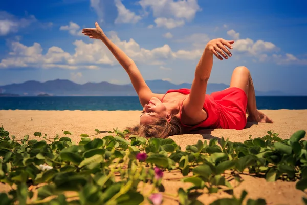 Девушка в красном лежит на песке поднимает руки в сторону возле ползунков — стоковое фото