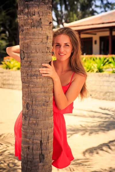 Blond girl in red leans out of palm — Stock Photo, Image