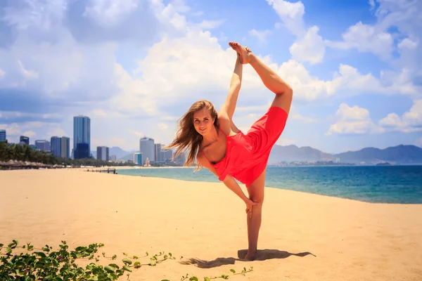Sarışın kız kırmızı jimnastik pozisyon bacak ölçek kum üzerinde duruyor — Stok fotoğraf