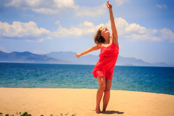 Chica rubia en puestos rojos en la playa de arena levanta la mano apunta al sol —  Fotos de Stock