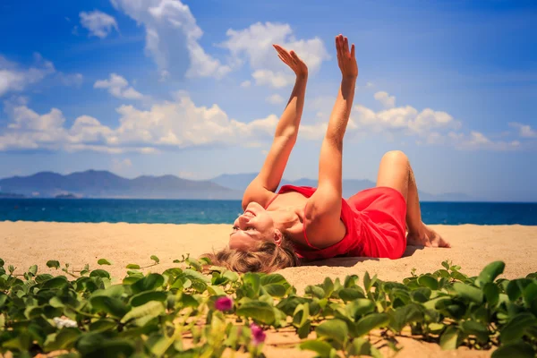 Dziewczyna w czerwonym leży na piasku podnosi ręce w pobliżu planie pnączy — Zdjęcie stockowe