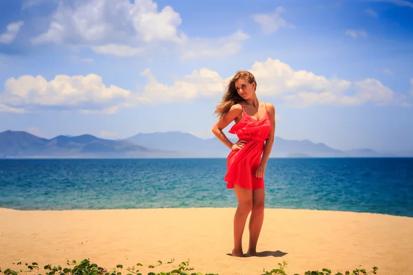 Blonde fille en rouge se tient sur le sable tient la main sur la hanche à midi — Photo