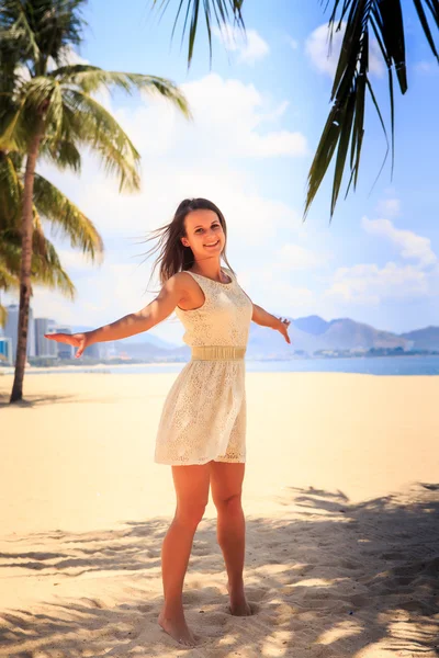 Стройная девушка в белом платье позирует с руками в сторону на пляже — стоковое фото