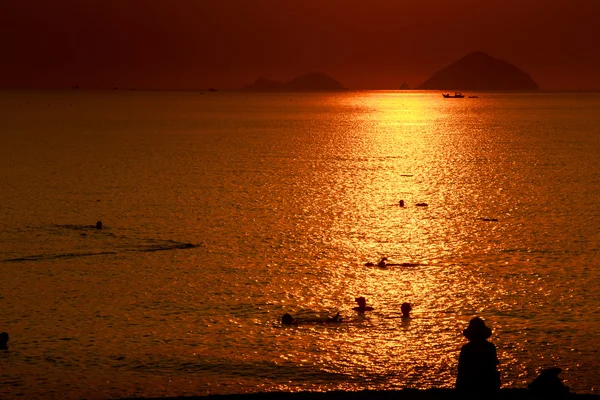 Människor silhuetter över solnedgången över havet — Stockfoto