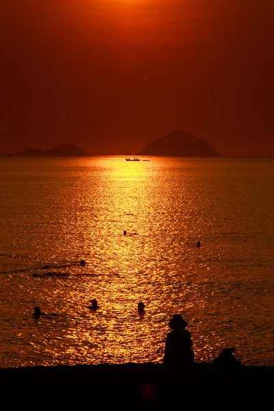 Pessoas silhuetas sobre o pôr do sol acima do mar — Fotografia de Stock