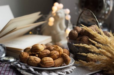 Kareli bir masa örtüsünün üzerindeki metal tepside ceviz şeklinde kurabiyeler, yanında vazodaki bir kabuk, açık bir kitap, bir saat, bir mermer ayı. Kış tatili kurabiyeleri