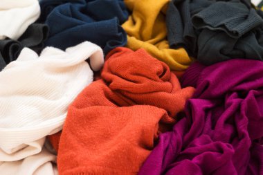 Bir sürü örgü süveter etrafa saçılmış. Parlak renkli kadın süveterleri dağınık, arka planda yatıyor..