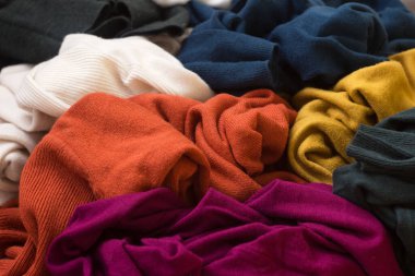 Bir sürü örgü süveter etrafa saçılmış. Parlak renkli kadın süveterleri dağınık, arka planda yatıyor..