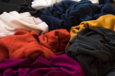 Bir sürü örgü süveter etrafa saçılmış. Parlak renkli kadın süveterleri dağınık, arka planda yatıyor..