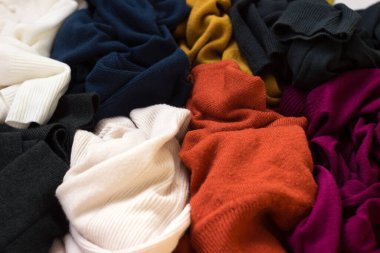 Bir sürü örgü süveter etrafa saçılmış. Parlak renkli kadın süveterleri dağınık, arka planda yatıyor..