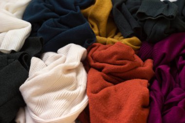 Bir sürü örgü süveter etrafa saçılmış. Parlak renkli kadın süveterleri dağınık, arka planda yatıyor..