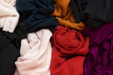 Bir sürü örgü süveter etrafa saçılmış. Parlak renkli kadın süveterleri dağınık, arka planda yatıyor..