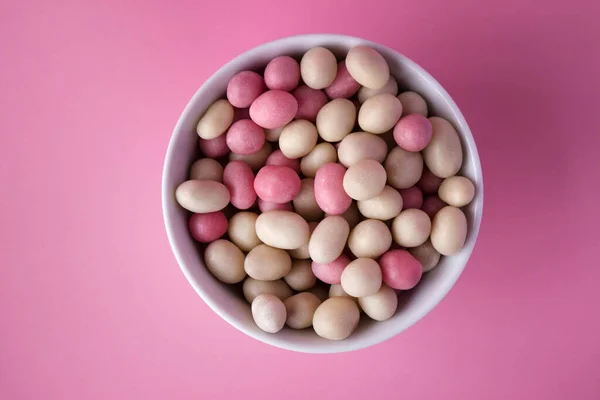 釉料中的白色和粉色圆形糖果 里面有花生 放在粉红背景的盘子里 从上面看 — 图库照片