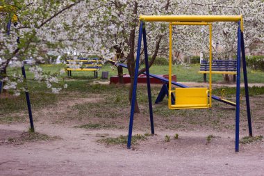 Boş çocuk parkı, salıncaklar ve çiçek açan ağaçlar. Küçük çiçekli bir sürü ağaç, arka plan