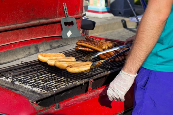 A man is grilling buns and hot dog sausages. Cooking street food on a homemade grill from the hood of a car