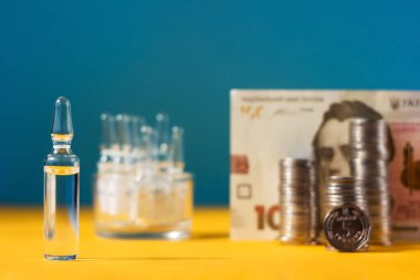 Birçok ampul aşı ve Ukrayna 100 Hryvnia banknotu ve sarı-mavi arka planda madeni paralar. Tıp konsepti