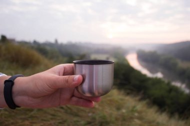 Bir adam sabahın köründe elinde metal bir kupa tutuyor. Şafakla nehir arasında. Seyahat kavramı