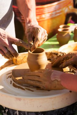 Yetişkin bir öğretmen, kilden sürahi yapmada yüksek lisans yapıyor. Çocuğa kilden ürün yapmayı öğretiyor.