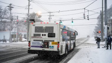NORWALK, CT, USA - FEBRUARY 13, 2024: Snowstorm in February 2024 on East Coast. Public transportation bus passing on Post Road during heavy snowing and people waiting for bus.
