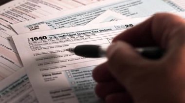 ABD vergi formlarını evdeki bir ofiste yazan kişi. Bireyler gelir vergisi iadelerini 2025 yılı için hazırlıyorlar. Formlar arasında gelir ve kesintiler hakkında bilgi yer alıyor.