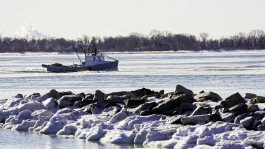 NORWALK, CT, ABD - 30 Ocak 2026: Buzlu suda bir tekne hareket ediyor ve buzu eziyor... balıkçılar çalışmalarına devam ediyor sahnenin sahil boyunca kayalar ve buzlar görünüyor..