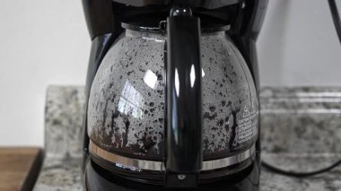 Otomatik damlayan kahve makinesindeki cam demliği dolduran taze demlenmiş kahve. Modern bir mutfak aletinde hazırlanan sıcak bir içecek.