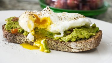 Taze avokado tostu ve mükemmel haşlanmış yumurta. Yumurtanın sarısı sağlıklı kahvaltı ekmeğinin üzerine dökülüyor.