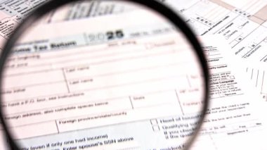 Bir kişi çeşitli vergi belgelerini ve 1040 yılını büyüteçle inceliyor. Konferansta rakamlar ve vergi dosyalarıyla ilgili bölümler üzerinde duruluyor. Evdeki vergi sezonunda gerçekleşir..