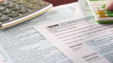 Vergi mükelleflerinin eli, vergi sezonu için Birleşik Devletler bireysel gelir vergisi iadesi formunu doldurmak için bir hesap makinesi kullanıyor.