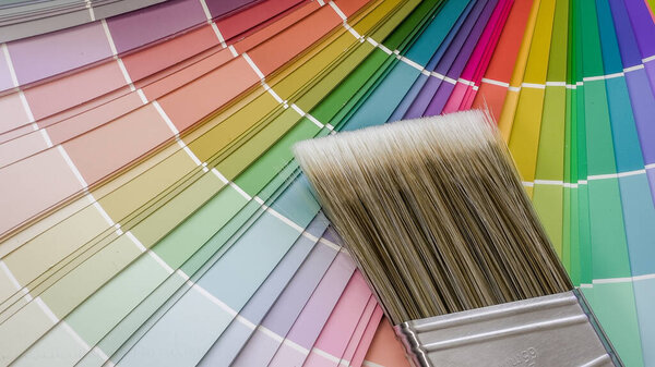 Paintbrush lying on a vibrant fan deck, displaying various color swatches for home renovation, interior design, and art projects