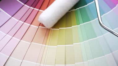 Duvar boyası seçmek için renk numunelerinden oluşan bir yelpazenin üzerinden geçen bir boya silindirinin yakın çekimi. Ev geliştirme ve yenileme konsepti
