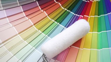 Yeni bir boya rulosu ve temiz bir fırça da dahil olmak üzere boyama araçları, ev yenileme için canlı bir yelpazeli renk rehberi üzerinde yatıyor